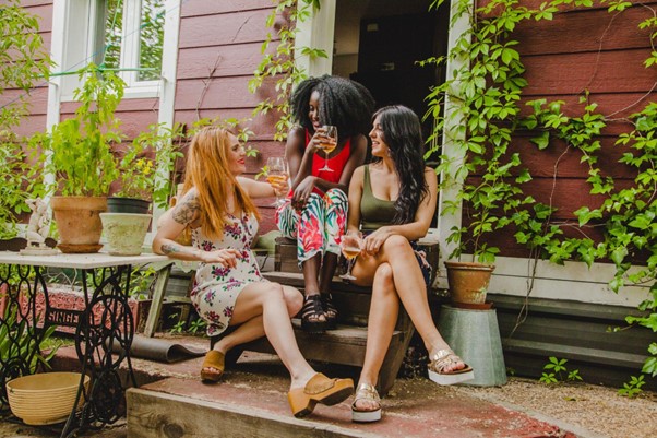 [Obrázok: Tri ženy sedia na schodoch domu, vychutnávajú nápoje a rozprávajú sa. Sú obklopené rastlinami a zeleňou. (freepik)]